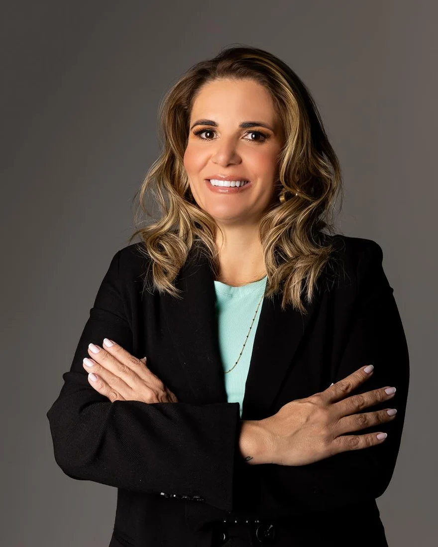 Dra. Dângela Costa, advogada, de blazer preto e braços cruzados